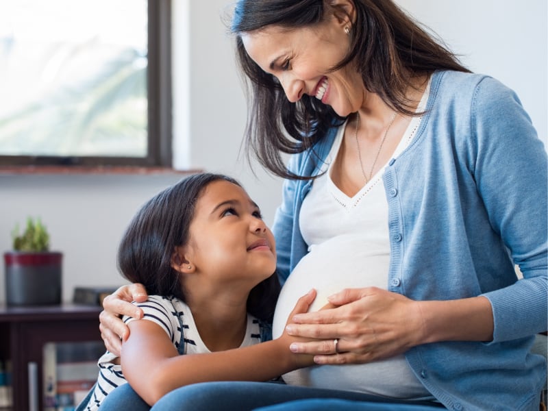 A young girl hugs her pregnant mother